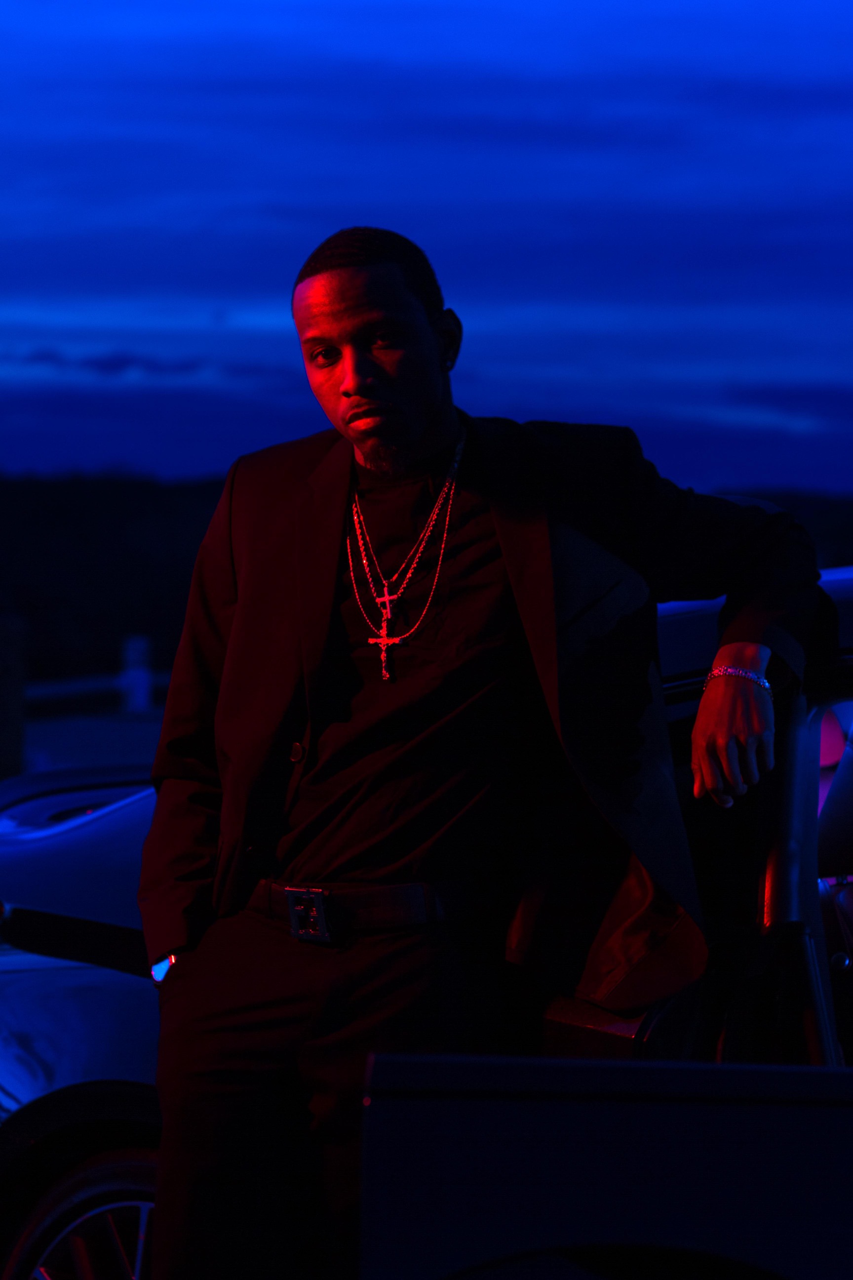 young man leans against a sports car during blue hour