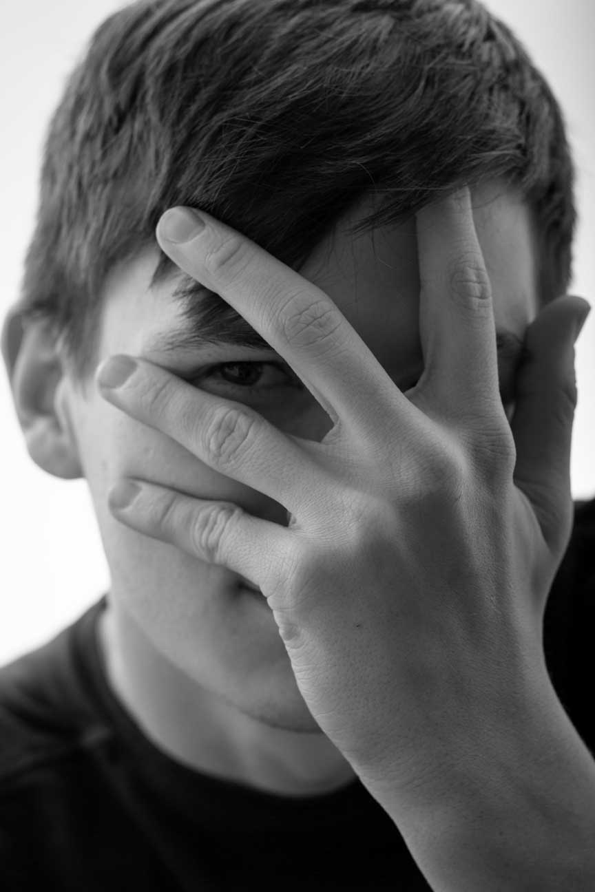 young man peeks between his fingers at the camera