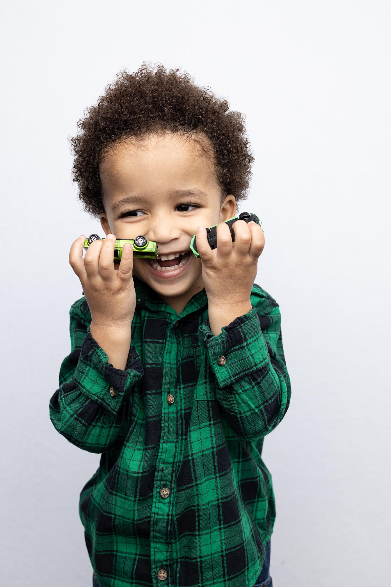 four year old boy smiles while holding his toy cars