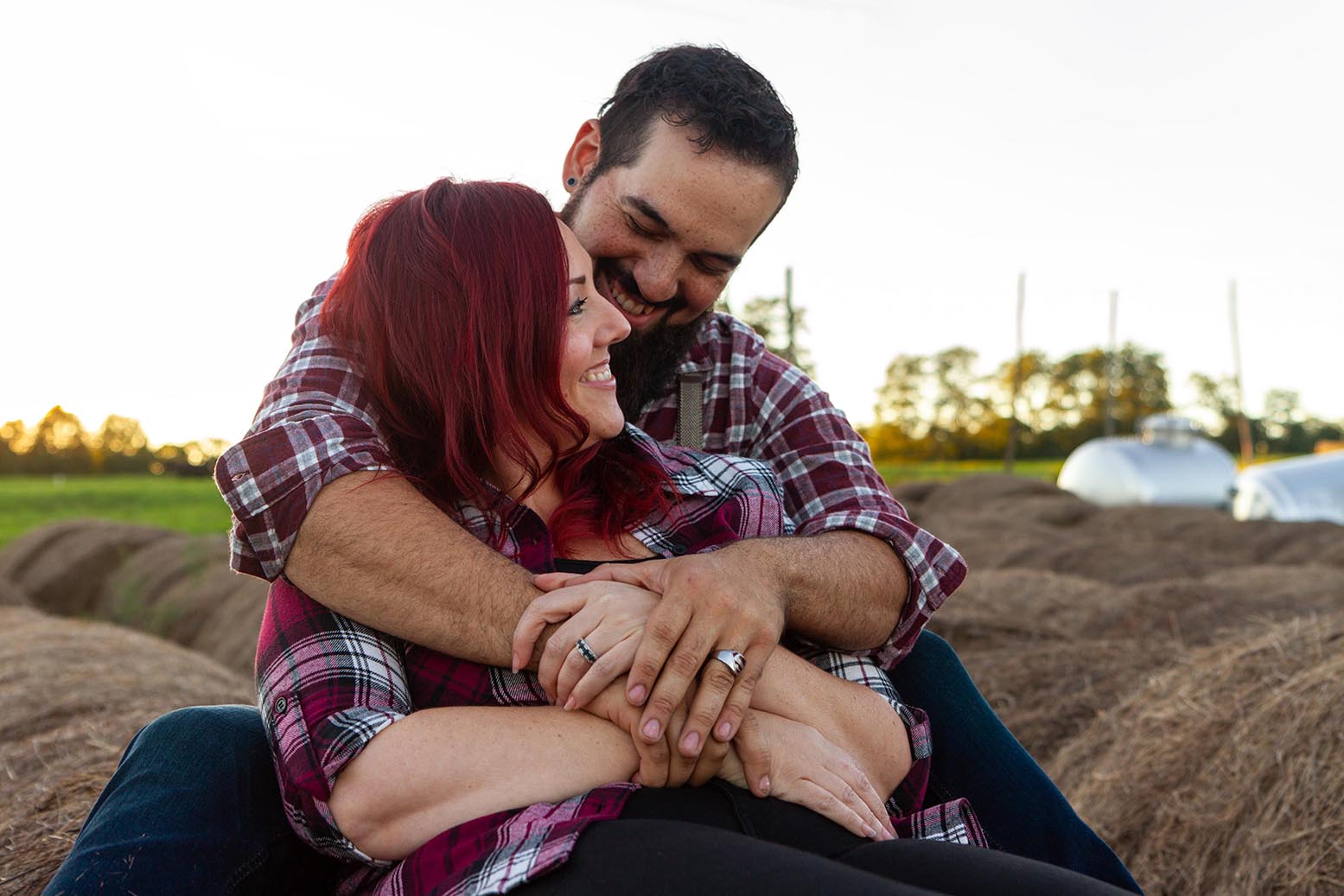 affianced couple smiles while sitting on a hay bale